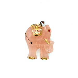 May include: A pink carved elephant pendant with gold accents and a red stone eye. The elephant is standing with its trunk raised.