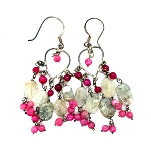 May include: Silver-tone dangle earrings with heart-shaped frames. The earrings feature a cascade of pink and red beads, along with clear and green-tinted oval-shaped stones. The earrings are designed for pierced ears.