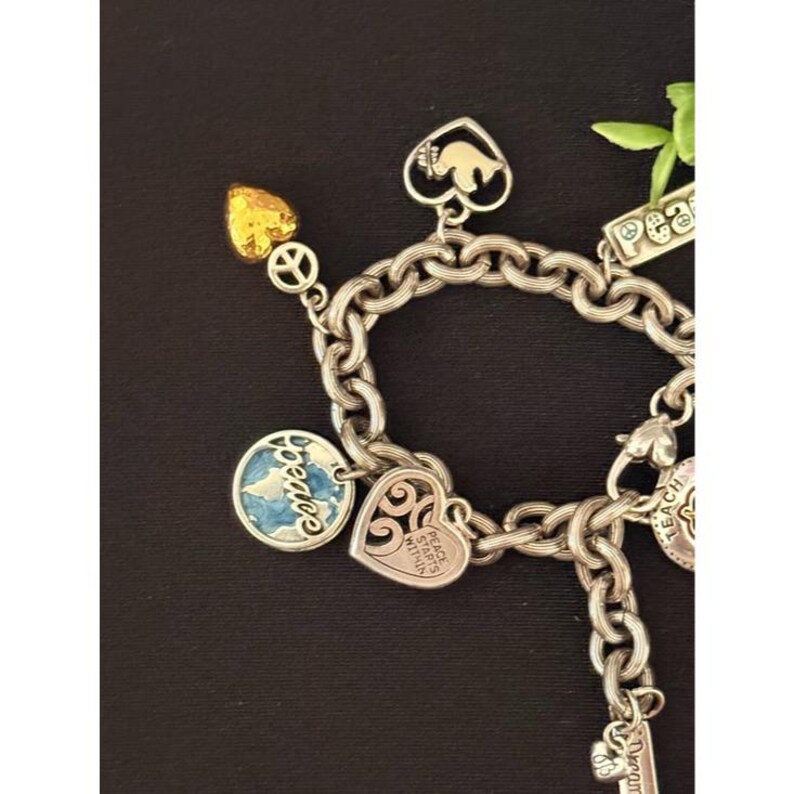 May include: Silver charm bracelet with various charms, including a peace sign, a heart with the words "Peace Starts Within", a globe, and a heart-shaped elephant. The bracelet has a chunky chain design and a gold-colored heart charm.
