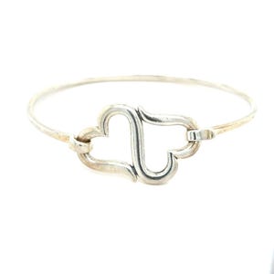 May include: A silver-toned bangle bracelet featuring two conjoined heart-shaped charms. The bracelet has a delicate, thin band and a clasp closure. The hearts are connected, creating a romantic and elegant design. The bracelet is set against a white background.