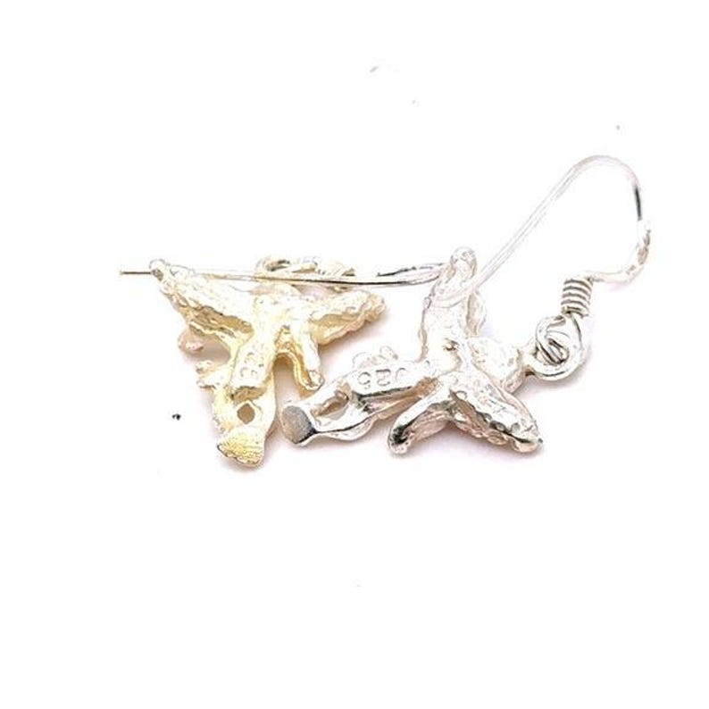 May include: A pair of silver-colored earrings with a coral-like design. The earrings have a hook closure and are set against a white background. The earrings are detailed with a textured surface.