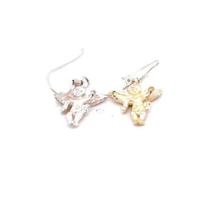 May include: A pair of angel-shaped earrings. One earring is silver-toned, the other is gold-toned. Each earring features a small cherub with outstretched wings, suspended from a curved ear wire. The earrings are set against a white background.