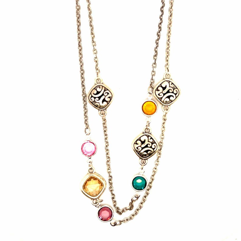 K&ouml;nnte beinhalten: Silberfarbene Halskette mit zwei Str&auml;ngen. Die Halskette hat quadratische Filigran-Anh&auml;nger und farbige, runde und quadratische Edelsteine in Rosa, Gelb, Orange und Gr&uuml;n. Die Halskette wird vor wei&szlig;em Hintergrund pr&auml;sentiert.