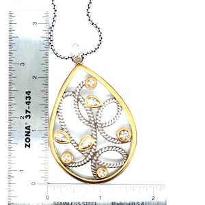 May include: A silver and gold-tone pendant necklace with a teardrop design. The pendant features a gold-tone border, silver-tone rope-like detailing, and clear gemstones. The pendant measures approximately 5 cm in length.
