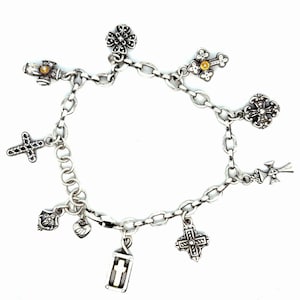 May include: A silver charm bracelet featuring various religious-themed charms, including crosses, a heart, and a lantern. The bracelet is made of linked chain and has a lobster claw clasp. The charms are detailed with intricate designs and embellishments.