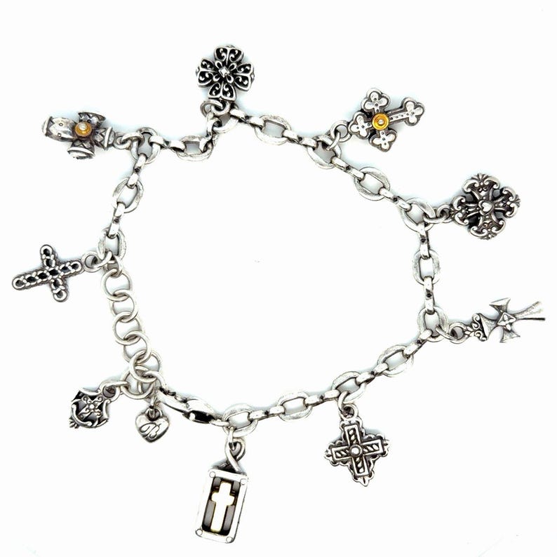 May include: A silver charm bracelet featuring various religious-themed charms, including crosses, a heart, and a lantern. The bracelet is made of linked chain and has a lobster claw clasp. The charms are detailed with intricate designs and embellishments.
