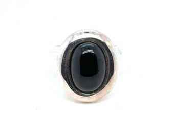 May include: A silver ring featuring a large, oval-shaped black stone. The stone is set in a bezel setting, and the ring has a simple, elegant design. The ring is shown against a white background.