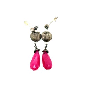May include: A pair of dangle earrings with silver-toned metal accents. Each earring features a faceted, hot pink teardrop-shaped stone suspended below a ribbed, silver-toned bead. The earrings have a post-back closure.