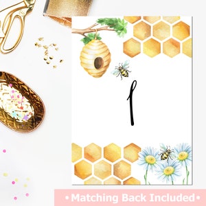 May include: A printable honeybee themed table number card with a watercolor illustration of a honeycomb, a beehive, and a bee. The number one is written in black script. The text "Matching Back Included" is at the bottom of the card.