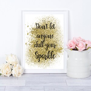 Op de afbeelding: Witte ingelijste print met gouden glitterachtergrond en zwarte tekst die "Laat niemand je glans dimmen" zegt.