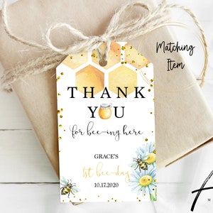 May include: A white thank you tag with a honeycomb pattern and gold glitter. The text reads "Thank You for bee-ing here."  It also includes the text "Grace's 1st bee-day 10.17.2020" and a bee and flower illustration.