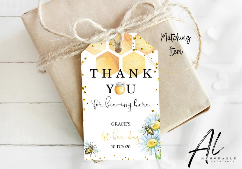 May include: A white thank you tag with a honeycomb pattern and gold glitter. The text reads "Thank You for bee-ing here."  It also includes the text "Grace's 1st bee-day 10.17.2020" and a bee and flower illustration.