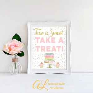 Może przedstawiać: Biały, oprawiony w ramę znak z tekstem "Two is Sweet Take a Treat!" w r&oacute;żowych i złotych literach. Znak zawiera akwarelową ilustrację tortu i babeczek z posypką.