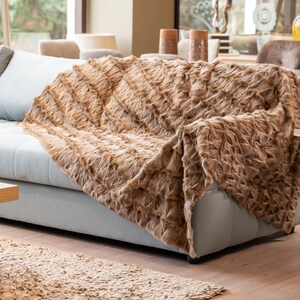 Op de afbeelding: Een bruine nep bont deken gedrapeerd over een lichtblauwe bank. De deken heeft een zachte, pluche textuur en is perfect om warmte en comfort toe te voegen aan elke woonkamer.