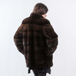 May include: A brown fur coat with a high collar and a quilted design. The coat is worn by a person with long brown hair.