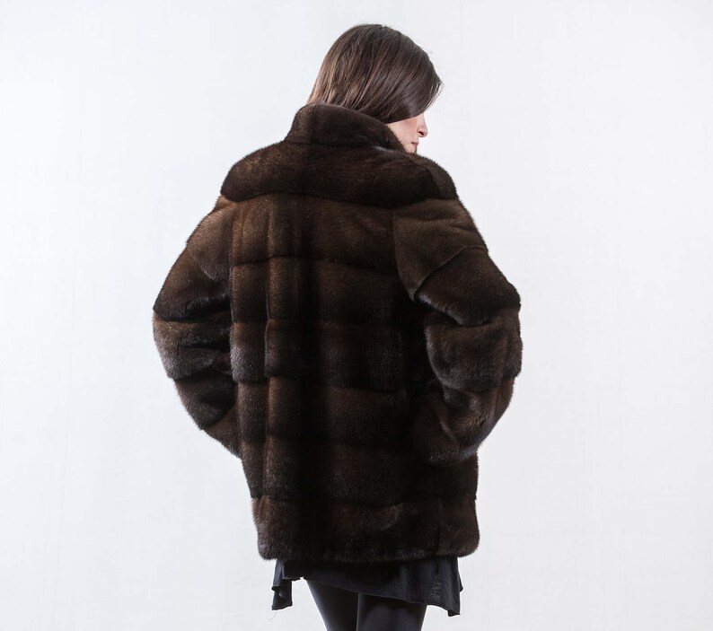 May include: A brown fur coat with a high collar and a quilted design. The coat is worn by a person with long brown hair.