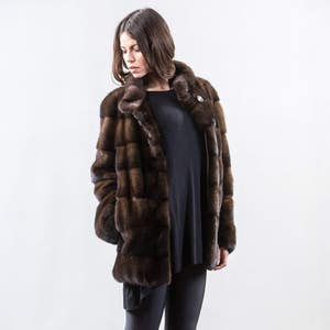 May include: A brown fur coat with a stand-up collar and a button closure. The coat is made of a soft, luxurious fur and has a sleek, modern design.