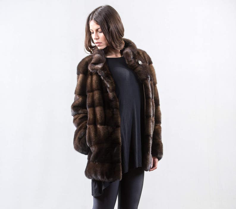 May include: A brown fur coat with a stand-up collar and a button closure. The coat is made of a soft, luxurious fur and has a sleek, modern design.