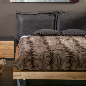 Op de afbeelding: Een bruine nep bont deken op een houten bedframe met bruine lederen hoofdkussens.