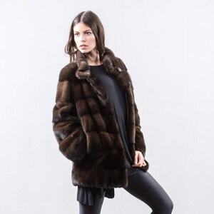 May include: A brown fur coat with a stand-up collar and a button closure. The coat is made of a soft, luxurious fur and has a sleek, modern design.