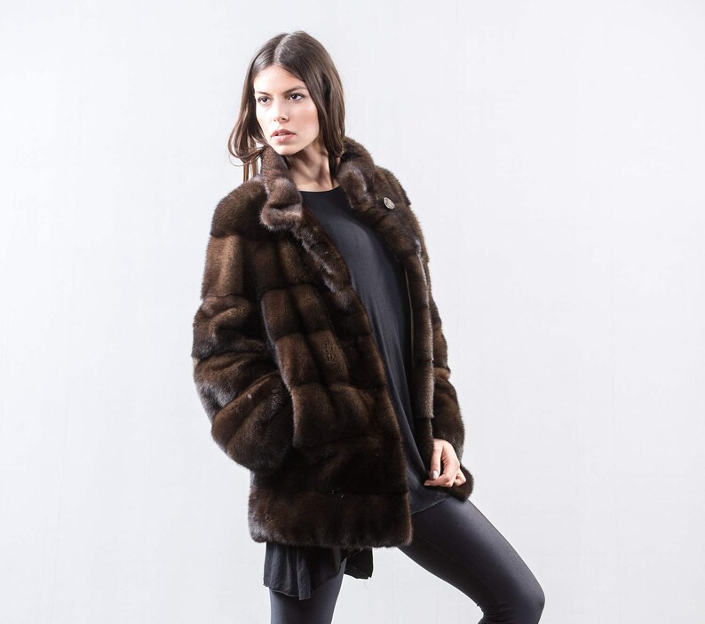 May include: A brown fur coat with a stand-up collar and a button closure. The coat is made of a soft, luxurious fur and has a sleek, modern design.