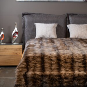 Op de afbeelding: Een bruine nep bont deken op een bed met twee witte kussens. De deken heeft een zachte, pluche textuur en is perfect om elke slaapkamer warmte en stijl te geven.