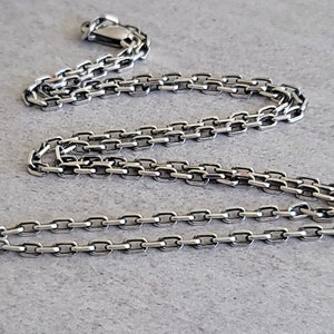 May include: A silver chain necklace with a box chain design. The chain is about 20 inches long and has a lobster claw clasp.
