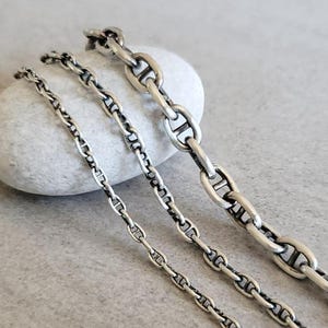 May include: Three silver mariner chain necklaces of different lengths. The chains are made of interlocking oval links.