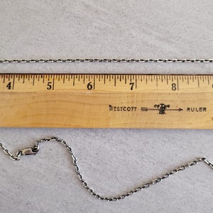 May include: A silver chain necklace measuring 9 inches long, laid out on a wooden ruler with the Westcott brand name and the word "ruler" printed on it.