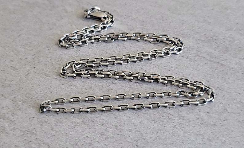 May include: A silver chain necklace with a box chain design. The chain is about 20 inches long and has a lobster claw clasp.