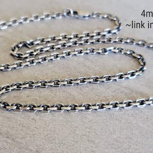 May include: A silver chain necklace with a 4mm chain. The chain is made of small, square links. The chain is lying on a light gray surface. 4mm Chain ~link in description