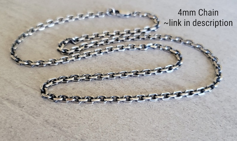May include: A silver chain necklace with a 4mm chain. The chain is made of small, square links. The chain is lying on a light gray surface. 4mm Chain ~link in description