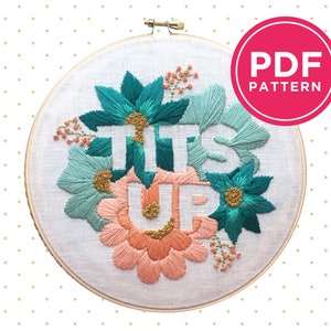Op de afbeelding: Een witte borduurring met een bloemenmotief en de woorden "ITS UP" geborduurd in groen en perzikkleurig garen.