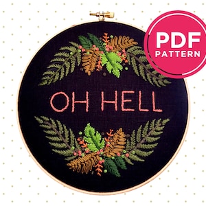 Peut inclure: Un cerceau de broderie noir avec un motif floral et le texte "OH HELL" en rose. Le cerceau est sur un fond blanc avec de petits points verts.