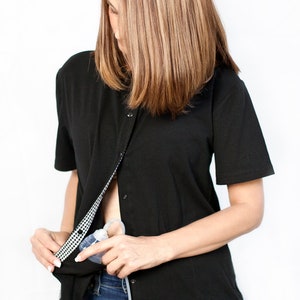 May include: A black button-down shirt with a white and black checkered pattern on the inside. The shirt is unbuttoned at the chest, revealing a clear medical device with a tube.