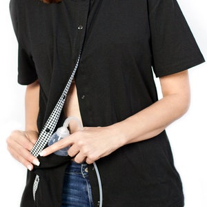 May include: Black short-sleeved nursing shirt with a button-up front. The shirt has a gingham-patterned lining and is designed for easy access for breastfeeding. A breast pump is visible.