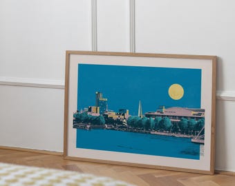 May include: A framed print of a cityscape with a blue sky and a large yellow moon. The cityscape features a tall building, a spire, and a bridge. The print is in a wooden frame.