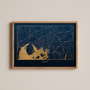 May include: A framed map of Oslo, Norway with gold foil accents. The map is printed on a dark blue background and shows the city's streets and waterways.