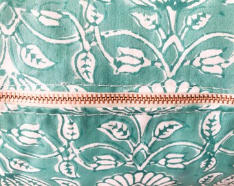 May include: A close-up of a zipper on a teal fabric with a white floral pattern. The zipper is made of gold metal.