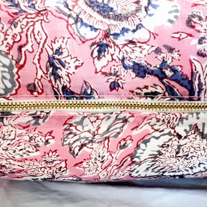 May include: A pink and white floral patterned pillow with a gold zipper. The pillow is made of a soft, cotton fabric and has a subtle sheen.