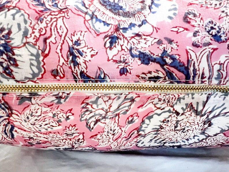 May include: A pink and white floral patterned pillow with a gold zipper. The pillow is made of a soft, cotton fabric and has a subtle sheen.