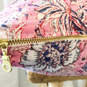 May include: A pink floral pillow with a gold zipper. The zipper has a pull tab with the letters "YKK" on it.