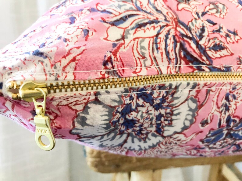 May include: A pink floral pillow with a gold zipper. The zipper has a pull tab with the letters "YKK" on it.