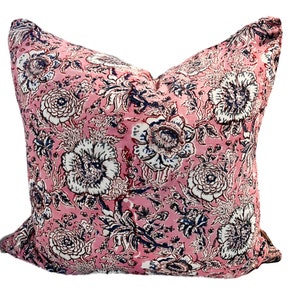 May include: A pink pillow with a floral pattern in shades of white, blue, and black. The pillow is made of a soft, cotton fabric and has a square shape.