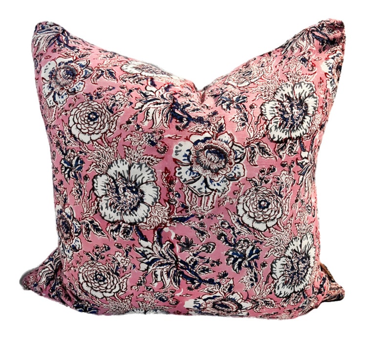 May include: A pink pillow with a floral pattern in shades of white, blue, and black. The pillow is made of a soft, cotton fabric and has a square shape.
