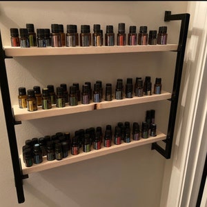 May include: A black metal shelf unit with three wooden shelves, each filled with rows of small glass bottles. The bottles are filled with colorful liquids and have black labels.
