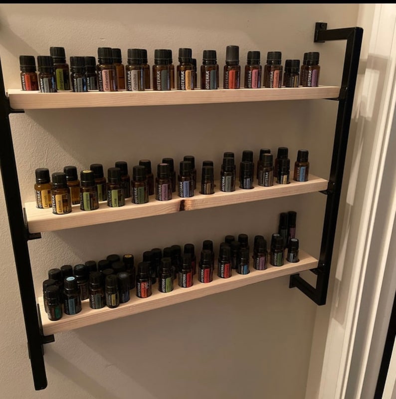 May include: A black metal shelf unit with three wooden shelves, each filled with rows of small glass bottles. The bottles are filled with colorful liquids and have black labels.