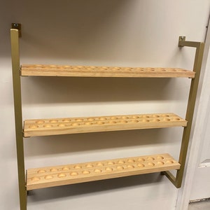 May include: A gold metal wall-mounted shelf with three wooden shelves. Each shelf has a series of evenly spaced circular holes.