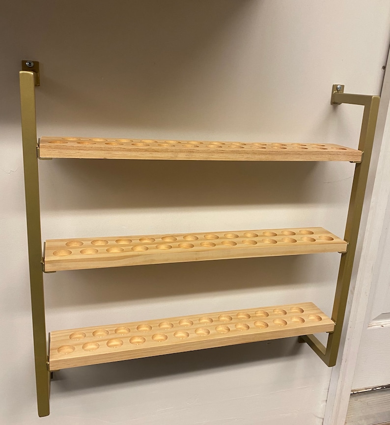 May include: A gold metal wall-mounted shelf with three wooden shelves. Each shelf has a series of evenly spaced circular holes.