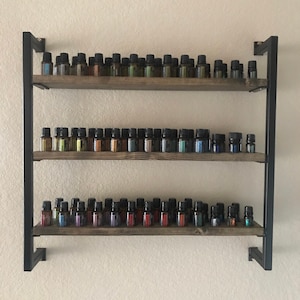 May include: A three-tiered wooden shelf unit with black metal framing. The shelves are filled with rows of small glass bottles, each with a different colored liquid inside.